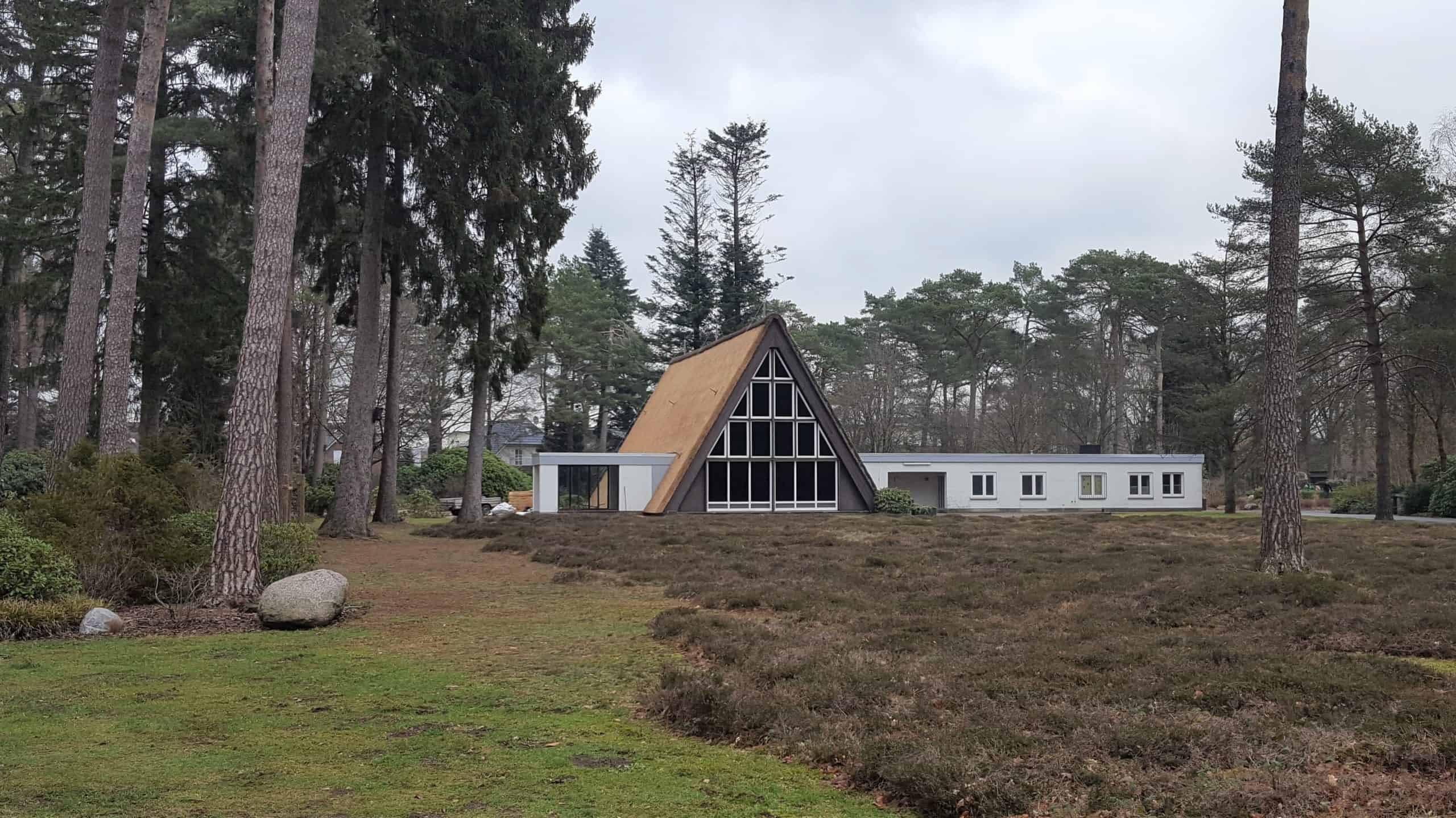 Modernes Haus mit Reetdach im Waldgebiet, umgeben von Bäumen.